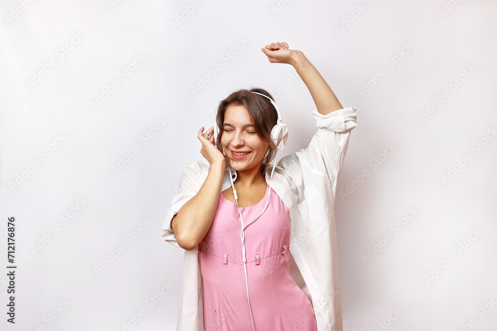 Beautiful cheerful girl in a pink suit and white shirt listens to music in headphones. Beautiful cheerful girl in a pink suit and white shirt listens to music in headphones.