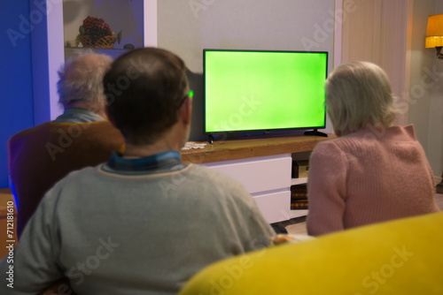 Family watching TV. Green screen. An elderly couple and their adult son are sitting on the couch at home and watching TV. In front of them is a green screen TV. 