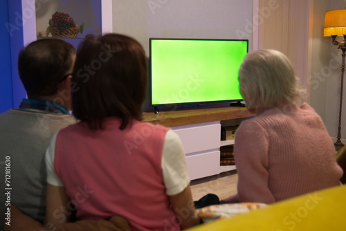 Family watching TV. Green screen. Middle-aged couple and grandmother are sitting on the couch at home. In front of them is a green screen TV. 