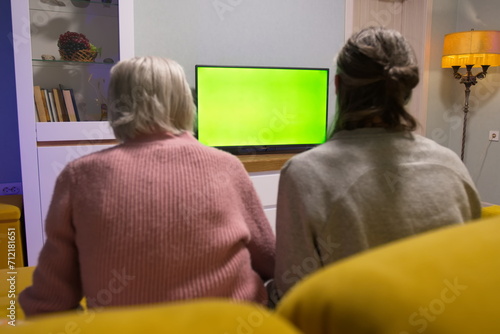 Family watching TV. Green screen. Grandmother and adult grandson are sitting on the couch. In front of them is a green screen TV. 