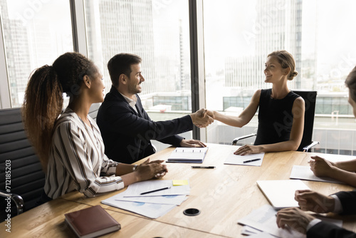 Successful young female business leader holding meeting with partners, investors, multiethnic team of colleagues, shaking hands with male manager, discussing agreement, corporate success