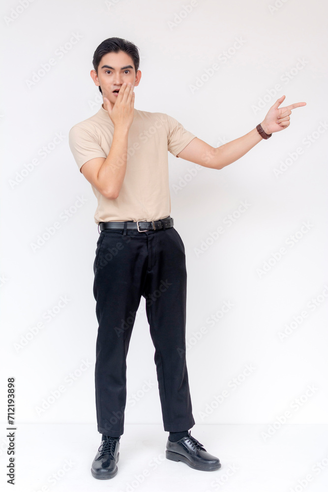 Startled young Asian man with a hand on his mouth and pointing to the side against a white backdrop. Startled young Asian man with a hand on his mouth and pointing to the side against a white backdrop.