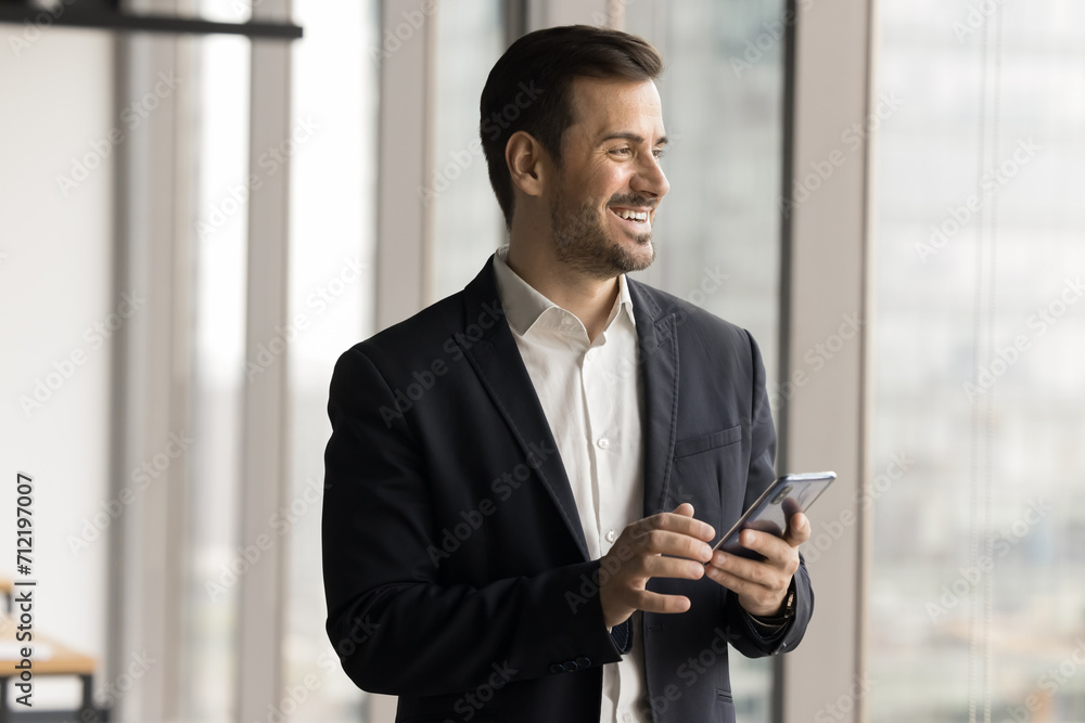 Happy confident entrepreneur man using mobile phone for business online communication, holding smartphone, looking at window away, thinking on wireless technology, smiling Happy confident entrepreneur man using mobile phone for business online communication, holding smartphone, looking at window away, thinking on wireless technology, smiling