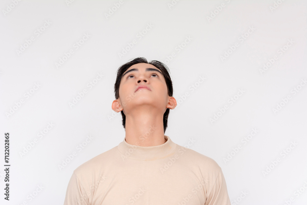 Portrait of a thoughtful young Asian man gazing upward against a neutral background, expressing contemplation. Portrait of a thoughtful young Asian man gazing upward against a neutral background, expressing contemplation.