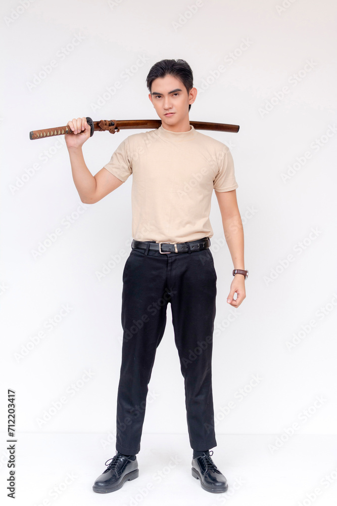 A young Asian man stands confidently with a traditional katana sword resting on his shoulder, exuding strength and determination.