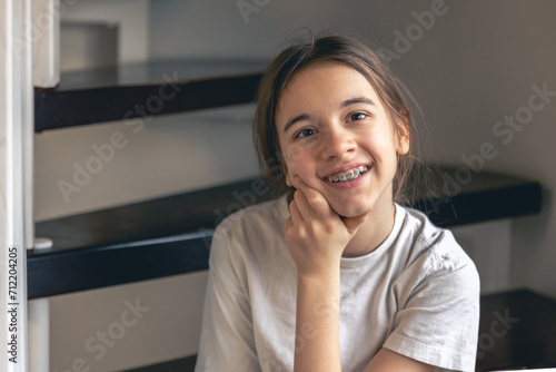 A teenage girl with braces smiles at home, showing her teeth.