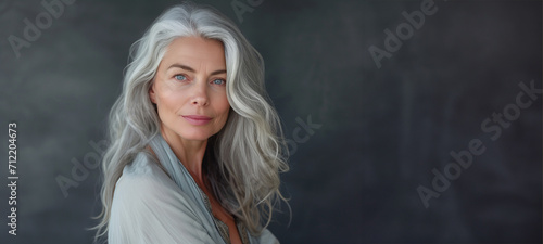 Close-up portrait of half face of cheerful middle-aged Asian 50s woman with silver gray long hair, attractive lady looks at camera and laughing. Mature model with naked shoulders isolated on brown photo