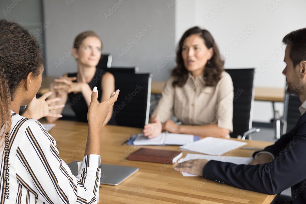 Cropped back view of young African American business woman sharing ideas with team of colleagues on office brainstorming meeting, discussing project management with elder colleague at table