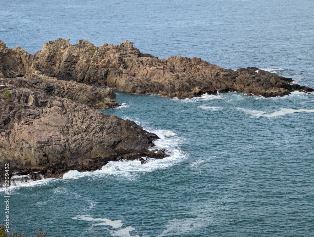 A rocky coast with waves crashing on the eroded rocks. The ocean is deep blue with white foam.