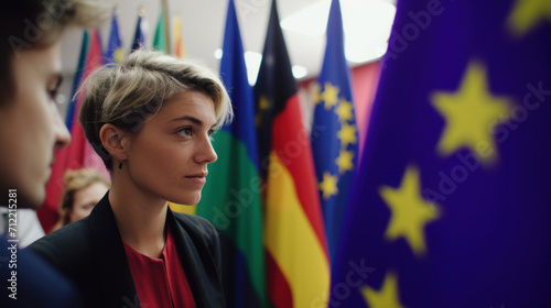 A contemplative young woman engages in discussion at a European Union event, surrounded by flags of member countries.