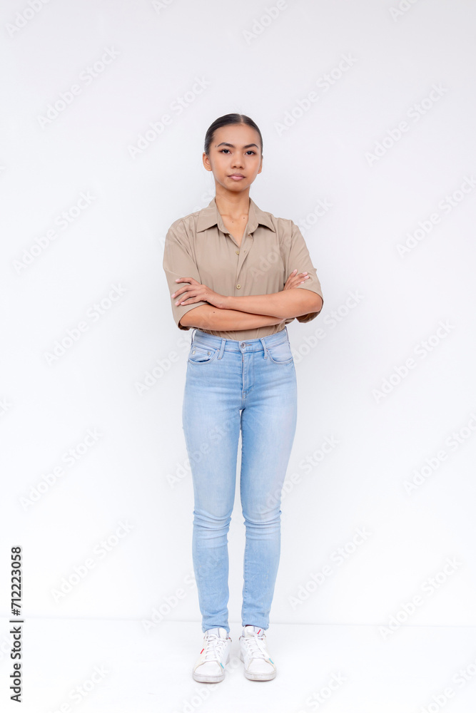 Portrait of a confident young Filipino woman with arms crossed, standing against a white background in casual attire. Portrait of a confident young Filipino woman with arms crossed, standing against a white background in casual attire.