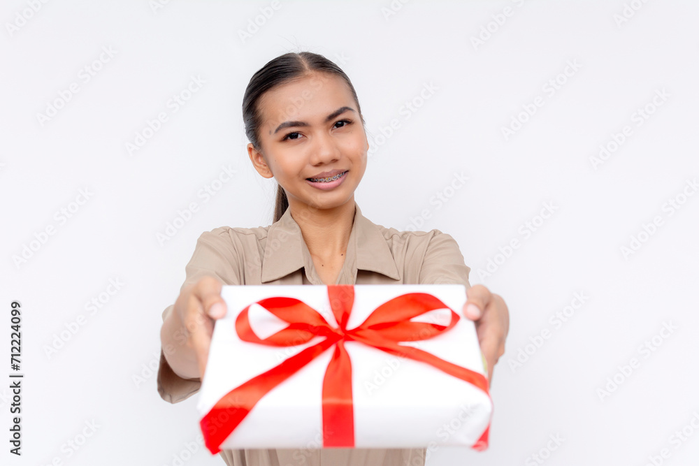 A young Filipino woman smiling as she offers a white gift with a red ribbon, expressing the joy of giving. Isolated on a white background. A young Filipino woman smiling as she offers a white gift with a red ribbon, expressing the joy of giving. Isolated on a white background.