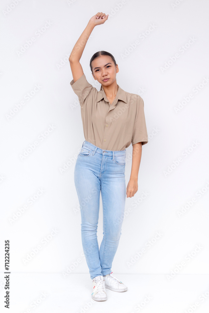 Portrait of a confident young Filipino woman in casual attire, standing with a relaxed raised arm against a white backdrop. Portrait of a confident young Filipino woman in casual attire, standing with a relaxed raised arm against a white backdrop.