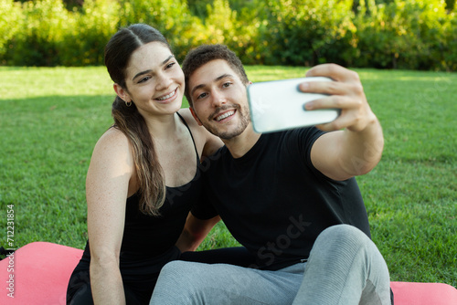 Pareja heterosexual caucasica enamorados haciendose un selfie en el cesped del parque posando sonrientes