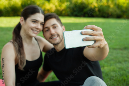 Pareja heterosexual caucasica enamorados haciendose un selfie en el cesped del parque posando sonrientes