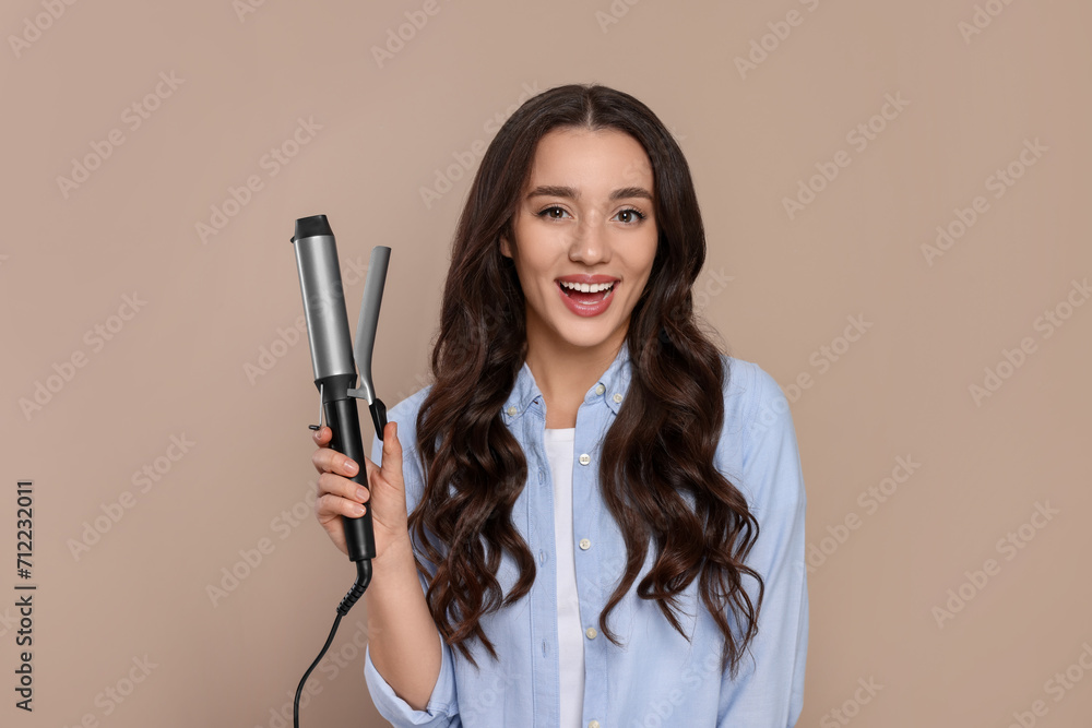 Happy woman with curling hair iron on beige background Happy woman with curling hair iron on beige background