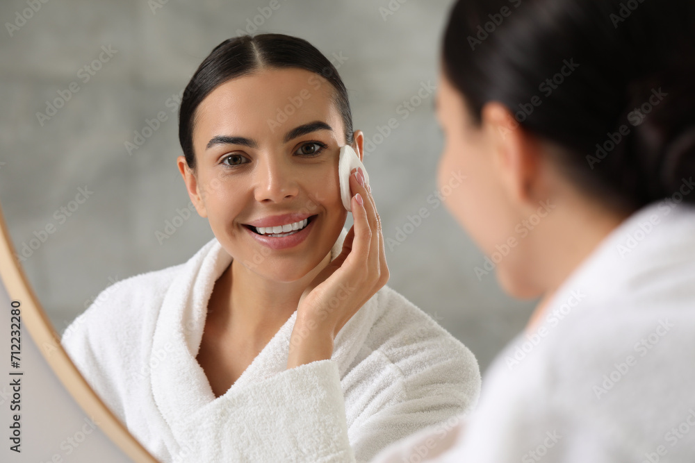 Beautiful woman removing makeup with cotton pad near mirror indoors Beautiful woman removing makeup with cotton pad near mirror indoors
