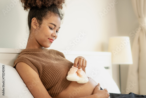 Joyful multiracial pregnant woman looking at her stomach expecting for childbirth. Young beautiful expectant mother relaxing on bed at home. Pregnancy and motherhood feminine anticipation lifestyle.