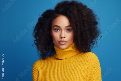Beautiful african american woman with curly hair in yellow sweater on blue background