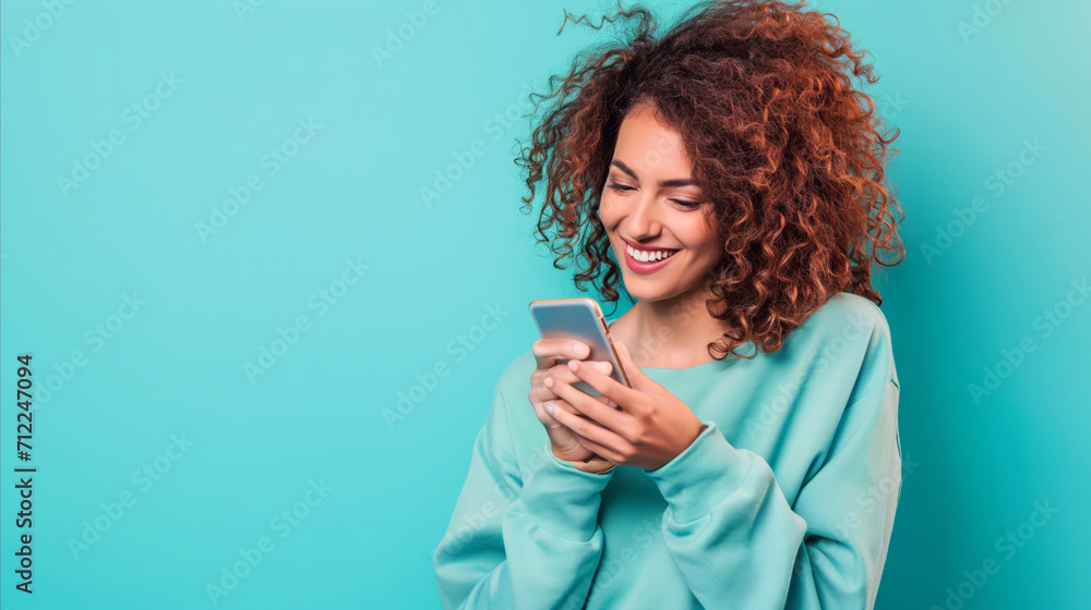 A woman smiles as she glances down at her cell phone, engrossed in its screen. A woman smiles as she glances down at her cell phone, engrossed in its screen.