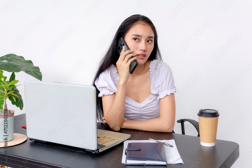 A dedicated young woman studies at her desk with a laptop, notebook, and coffee, while on a phone call. White background setting. A dedicated young woman studies at her desk with a laptop, notebook, and coffee, while on a phone call. White background setting.
