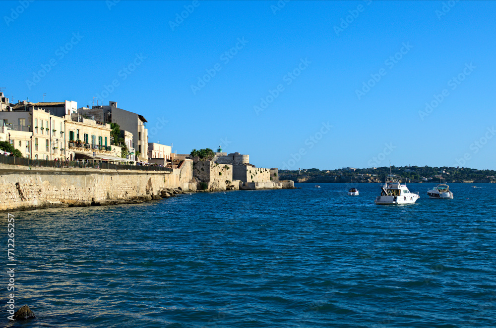 Scenic sunset landscape view of embankment in the oldtown in Syracuse, Sicily. Mediterranean sea with white moored motor boats. Blue sky background. Travel and tourism concept
