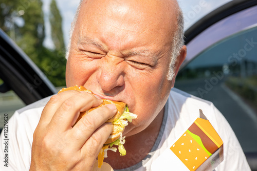 Grown man enjoying burger by the side of a car. The concept of fast food and takeaway food. Big juicy burger with cheese from McDonalds in the hand. Kiev, Ukraine, July 08 2023