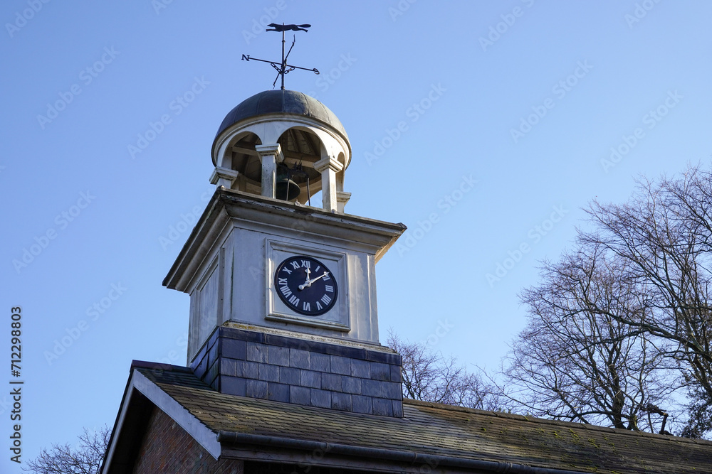Small clock tower on roof of building. time piece and weather vane 