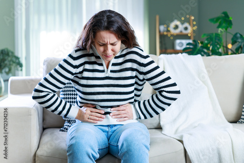 Young woman sitting on the couch at home with a pain in her stomach photo