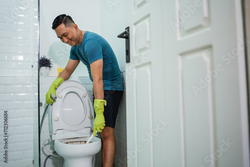 asian male wearing gloves cleaning toilet bowl in lavatory photo