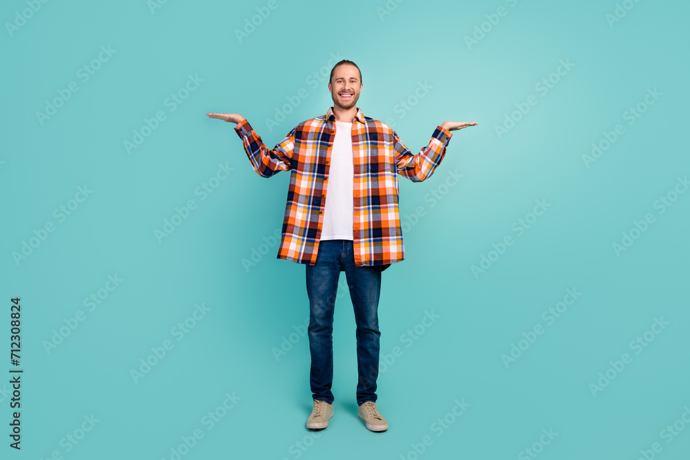 Full length photo of satisfied man wear flannel shirt jeans arms demonstrate objects empty space isolated on turquoise color background Full length photo of satisfied man wear flannel shirt jeans arms demonstrate objects empty space isolated on turquoise color background