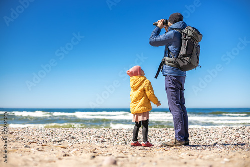 Bilde på lerret A tourist man standing on the seashore with his little daughter, using binocular