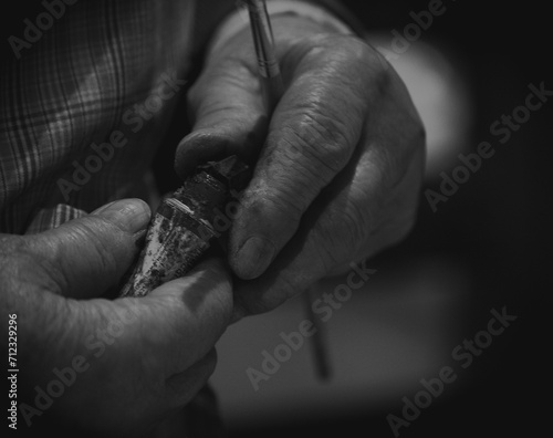 Imagen en blanco y negro de manos curtidas de la abuela preparando pintura para retocar un cuadro.
 photo