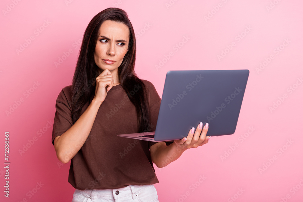 Photo of young funny business woman touch chin when brainstorm ponder look at laptop serious expression isolated on pink color background