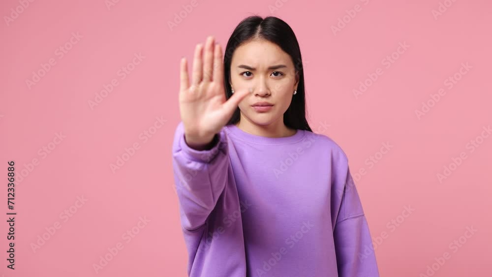 Serious strict severe young woman of Asian ethnicity wearing purple sweatshirt say no hold palm folded crossed hands in stop gesture isolated on plain pastel light pink background. Lifestyle concept Serious strict severe young woman of Asian ethnicity wearing purple sweatshirt say no hold palm folded crossed hands in stop gesture isolated on plain pastel light pink background. Lifestyle concept
