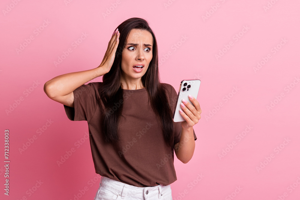 Portrait of young woman wearing brown t shirt confused hand touch head staring at smartphone cant login isolated on pink color background - obrazy, fototapety, plakaty 