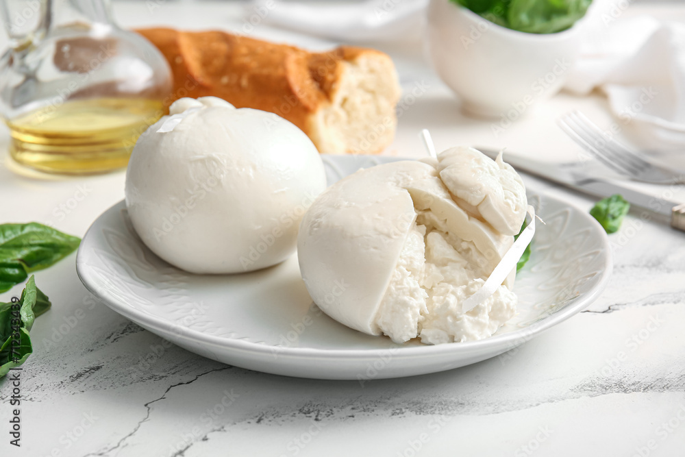 Plate of tasty Burrata cheese with basil and baguette on white background