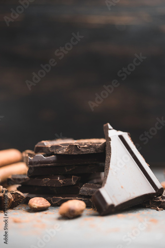 Heap of delicious dark chocolate pieces or cubes, chopped, broken chocolate bar, almond nut, cinnamon sticks and star anise on a dark background