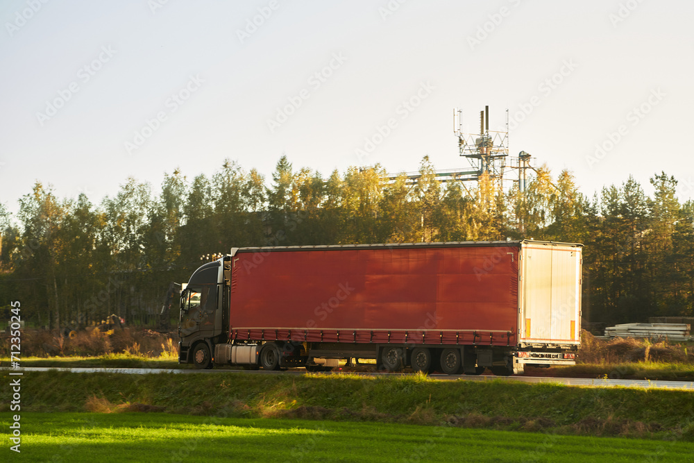 A red truck transports goods across a picturesque landscape illuminated by the golden hue of the setting sun. Truck transportation. A red truck transports goods across a picturesque landscape illuminated by the golden hue of the setting sun. Truck transportation.