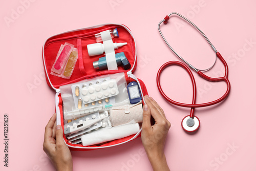 Female hands with first aid kit and pills on pink background photo