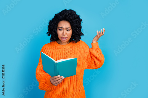 Photo of attractive young woman read book confused irritated dressed stylish knitted orange clothes isolated on blue color background photo