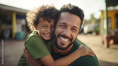 Homem brasileiro vestindo roupas verdes abraçando seu filho e sorrindo  photo
