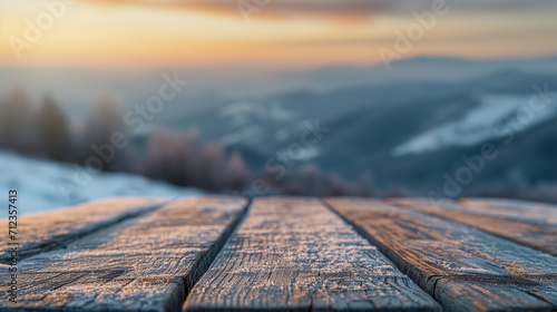 The empty wooden table top with snow and frost for your decoration of product or text and landscape of winter mountains with a small rural home and sunset time