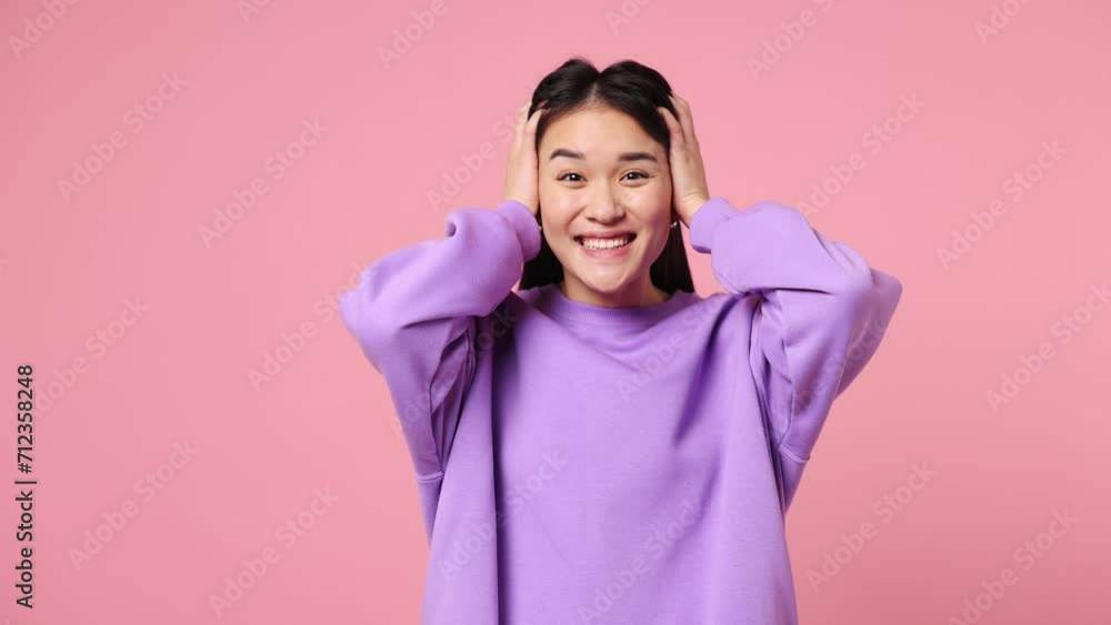 Young woman of Asian ethnicity wear purple sweatshirt look camera surprised ask what wow omg no way doing winner gesture say yes celebrating put hands on face isolated on plain pastel pink background Young woman of Asian ethnicity wear purple sweatshirt look camera surprised ask what wow omg no way doing winner gesture say yes celebrating put hands on face isolated on plain pastel pink background