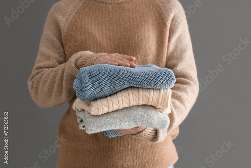 Woman holding stack of different stylish sweaters on grey background