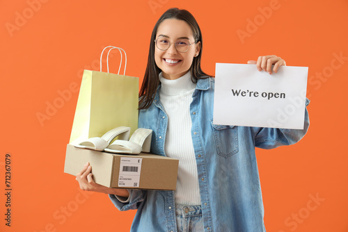 Female seller with OPEN sign, bag and shoe box on orange background © Pixel-Shot