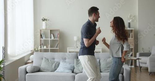 Excited attractive couple celebrating festive event, mortgage, anniversary, dancing in cozy spacious living room interior, singing song, having fun, enjoying motion, activity together photo