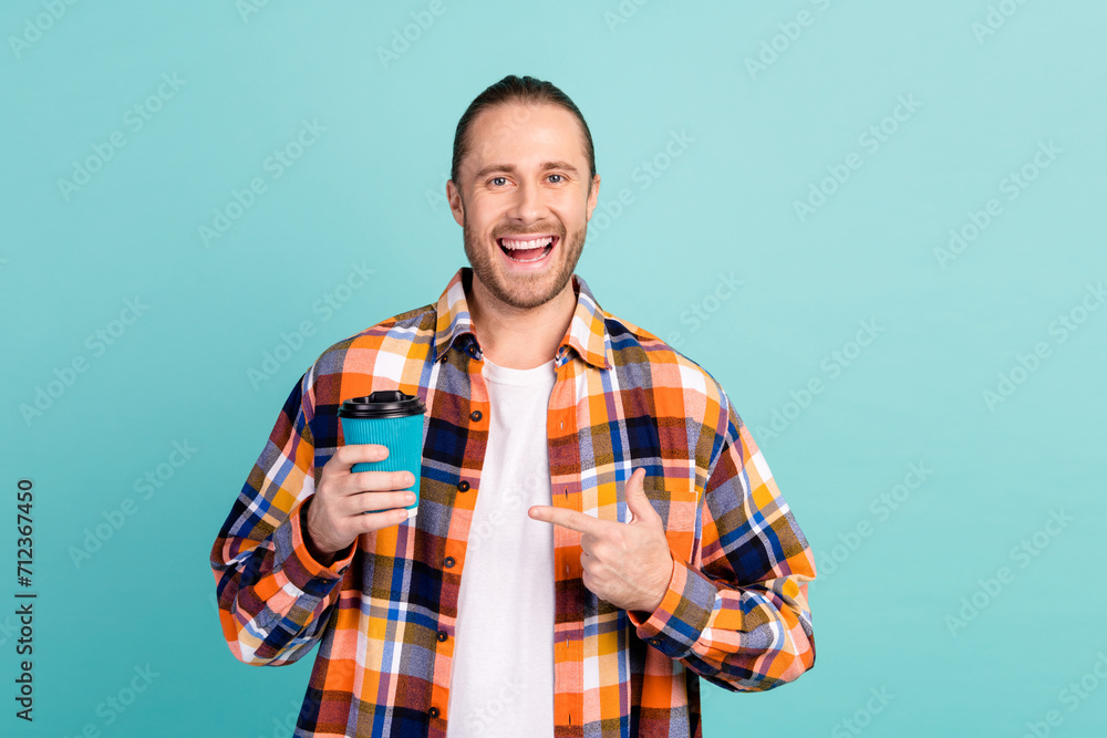 Portrait of overjoyed funny guy with stubble wear flannel shirt indicating at cup of hot latte isolated on turquoise color background Portrait of overjoyed funny guy with stubble wear flannel shirt indicating at cup of hot latte isolated on turquoise color background