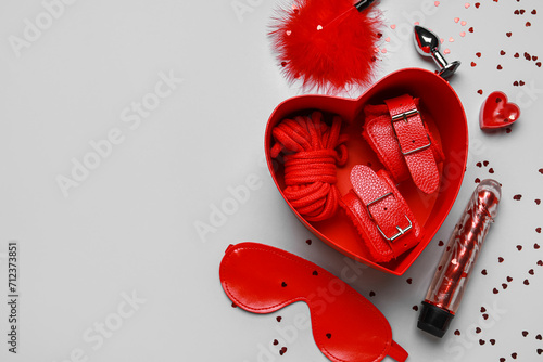 Gift box with different sex toys and confetti on grey background. Valentine's Day celebration photo