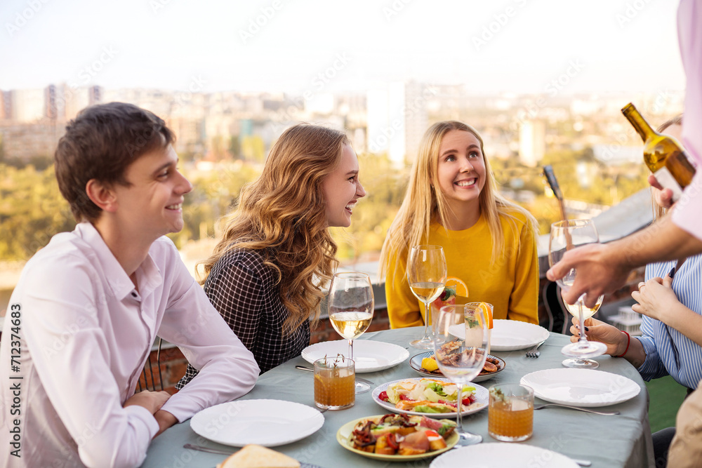Cheerful friends drinking white wine during roof party